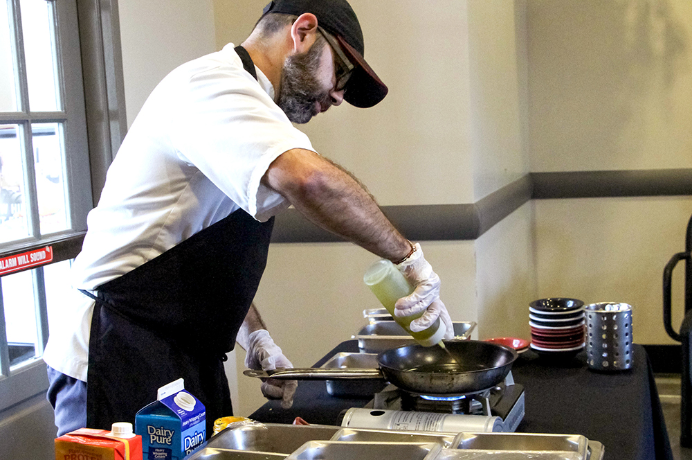 Chef adds oil to a pan during a demo.